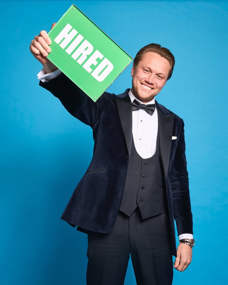 Man in tuxedo holding a sign that says "HIRED".