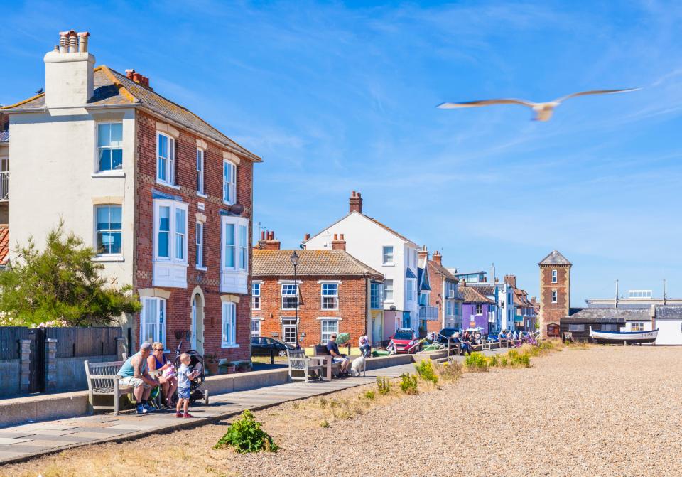 Aldeburgh beach in Suffolk, England, with Georgian houses and people relaxing on benches.