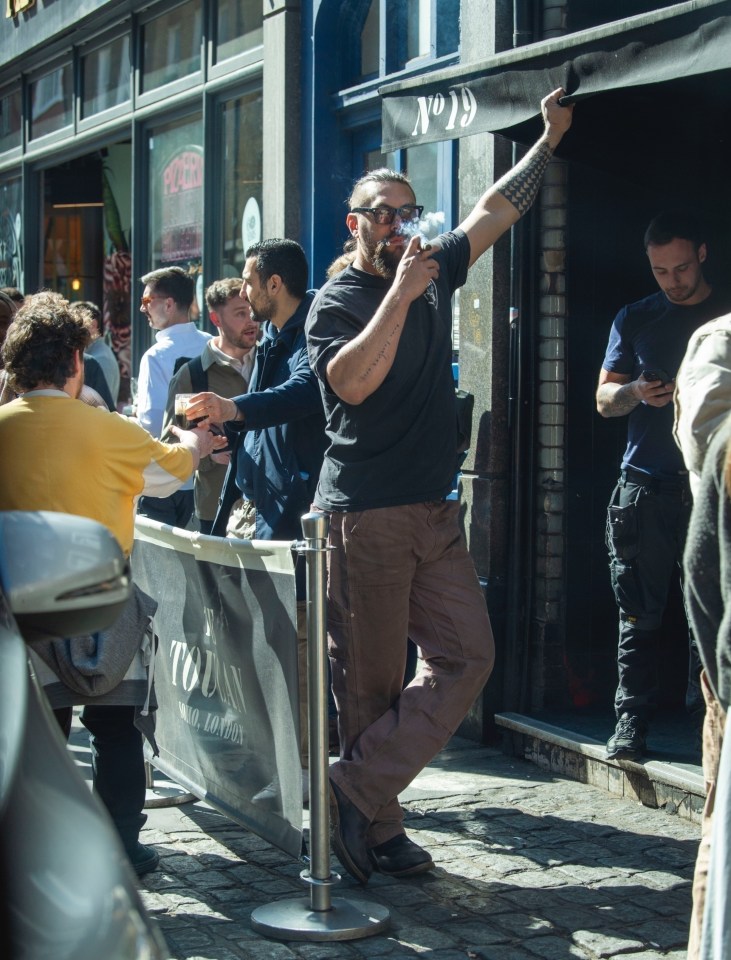 Jason Momoa smoking a cigar and drinking Guinness in London.