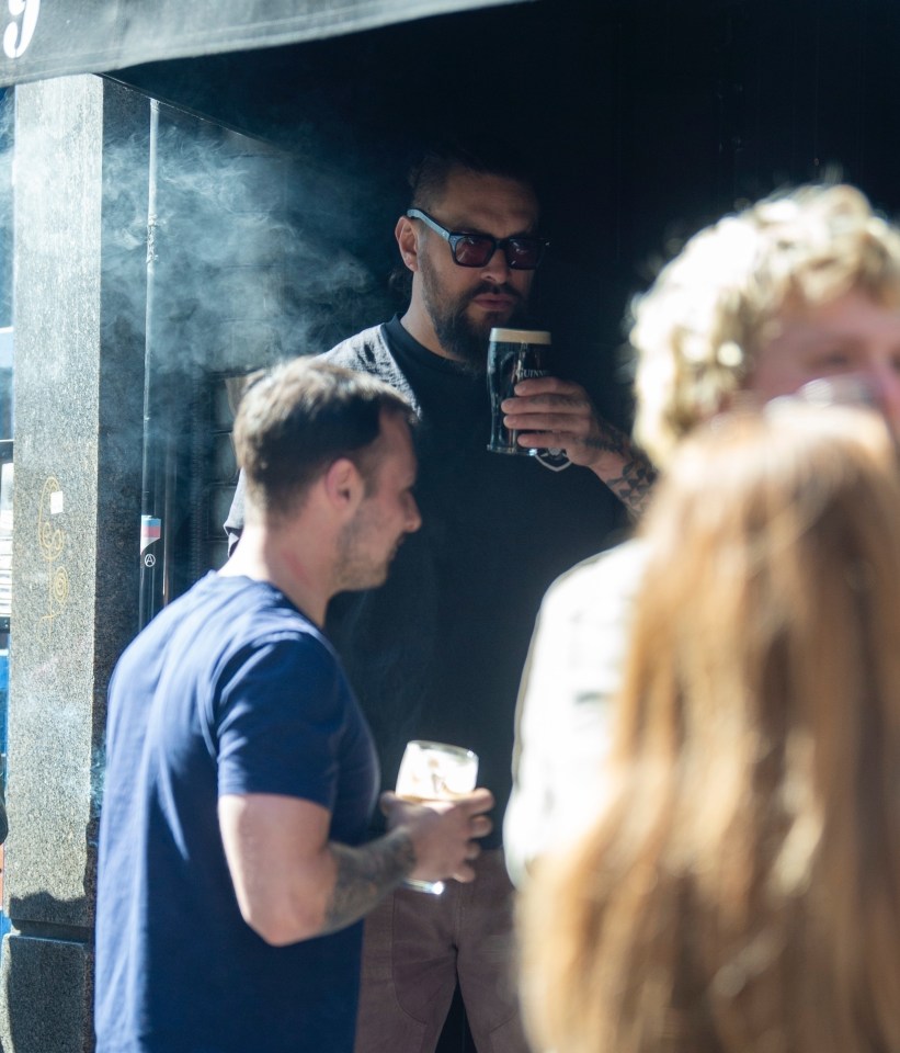 Jason Momoa smoking a cigar and drinking Guinness in London.