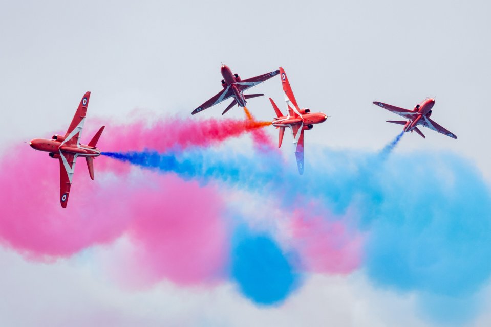 The Red Arrows performing in formation, leaving pink and blue smoke trails.