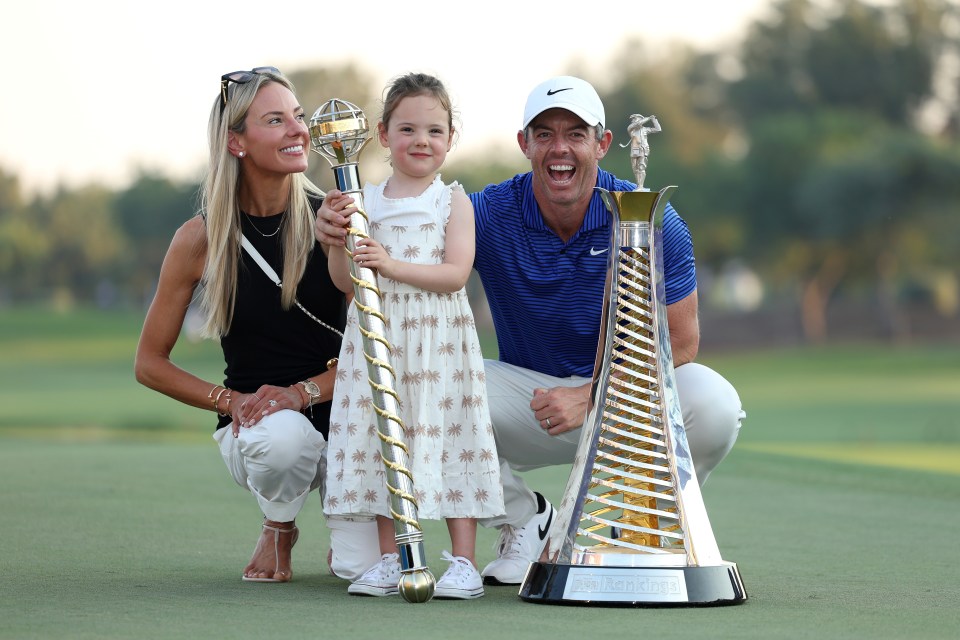 Rory McIlroy with his wife, daughter, and two golf trophies.