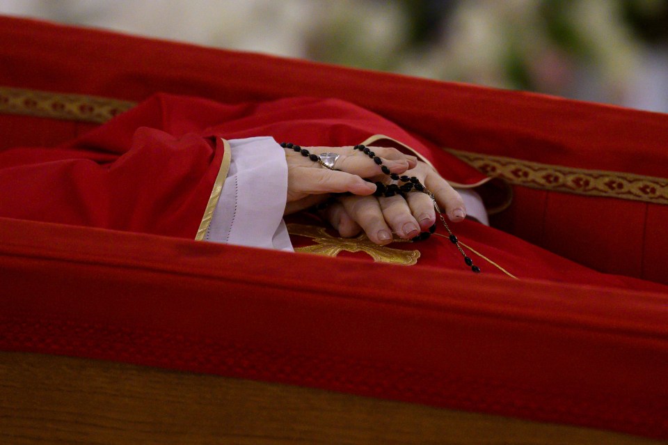 Pope Francis's hands holding a rosary in his open casket.