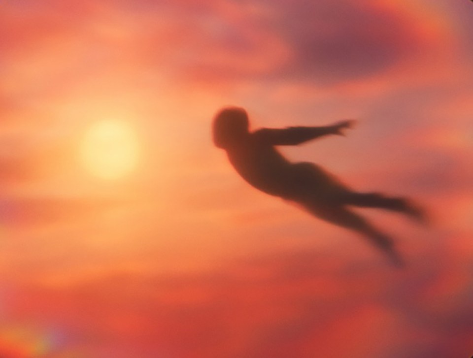 Blurry silhouette of a person flying in front of a sunset.