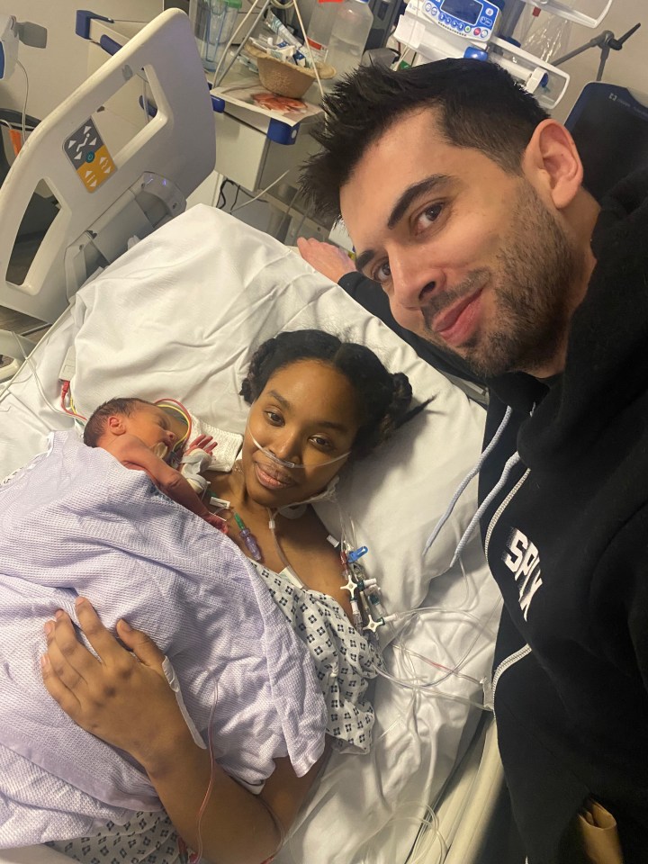 A postpartum mother and her newborn baby in a hospital bed, with the father next to them.