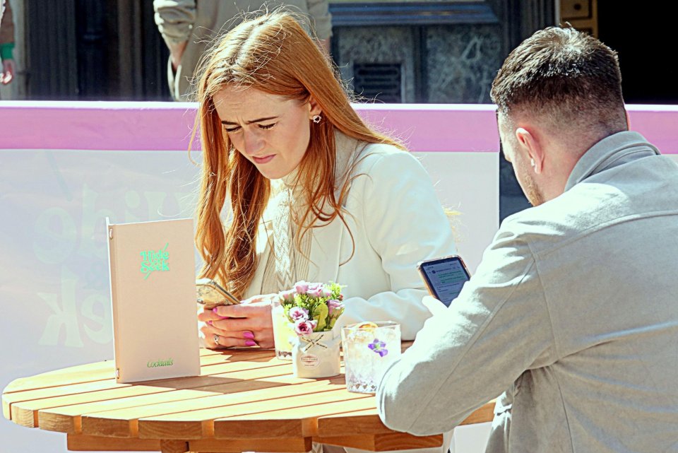 Two people sitting at a table outdoors, looking at their phones.