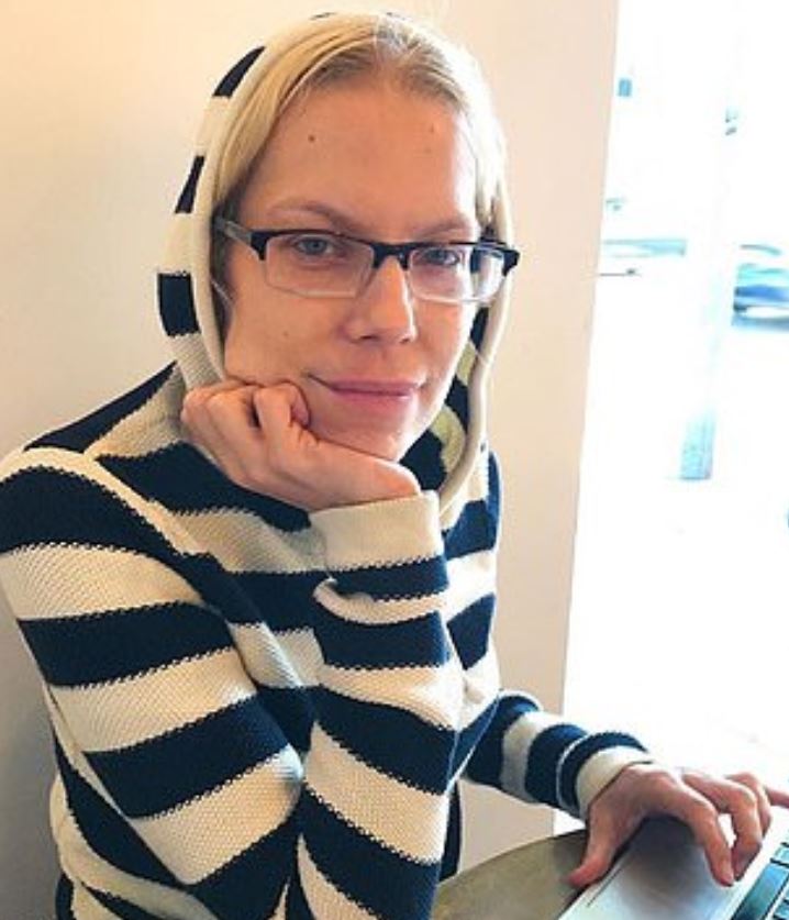 Woman wearing glasses and a striped hoodie, resting her chin on her hand.