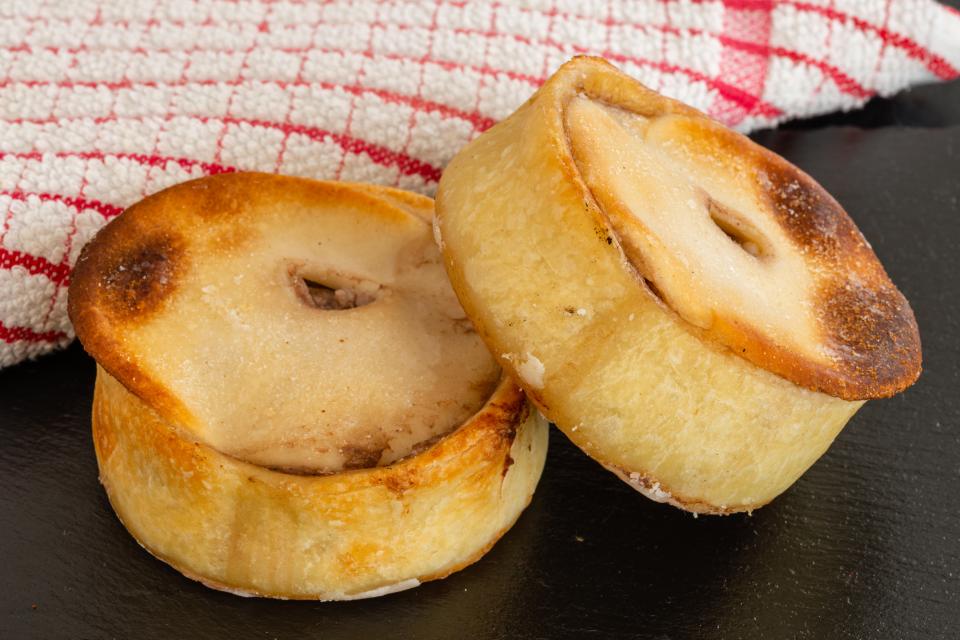 Two round Scotch pies on a black slate plate.