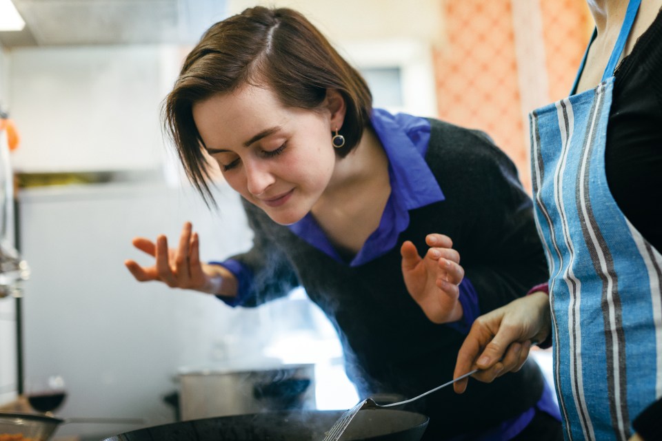 Woman smelling food cooking in a wok during a cooking class.