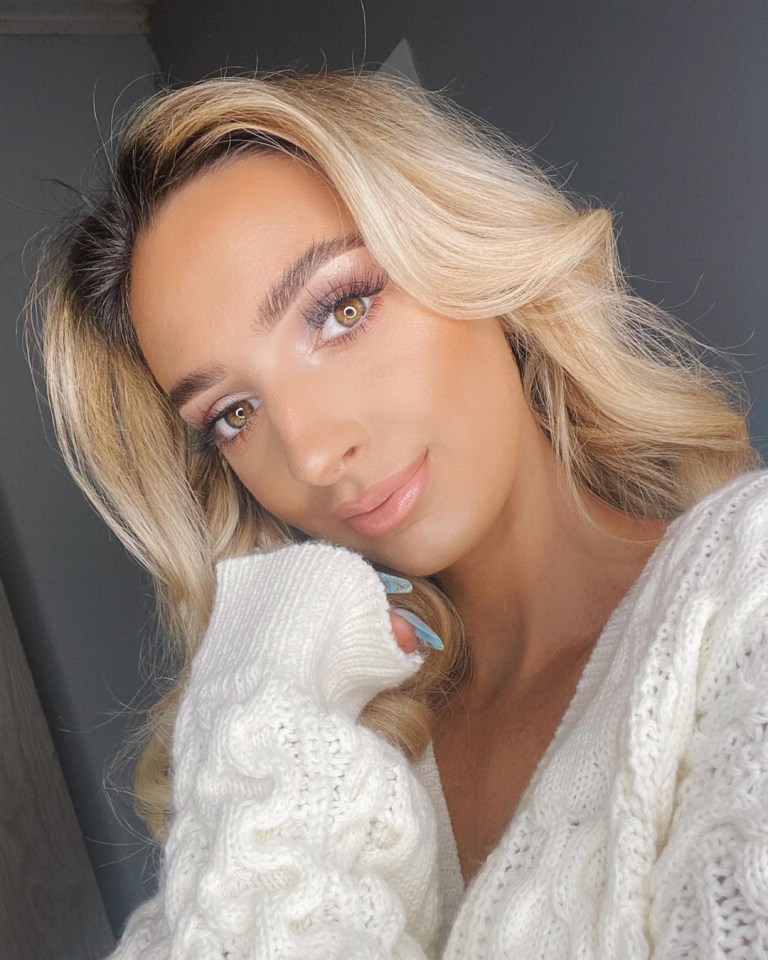 Close-up of a woman with blonde hair and makeup, wearing a white cable knit cardigan.