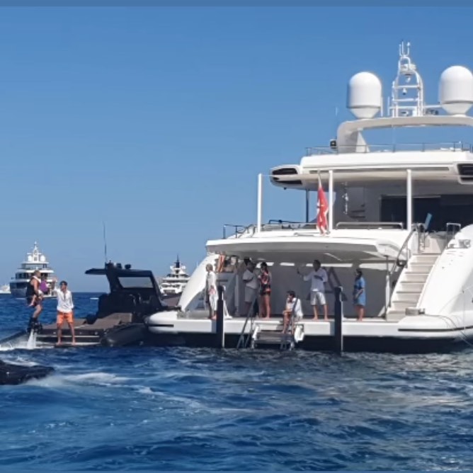 People on a flyboard near a large yacht and other boats.