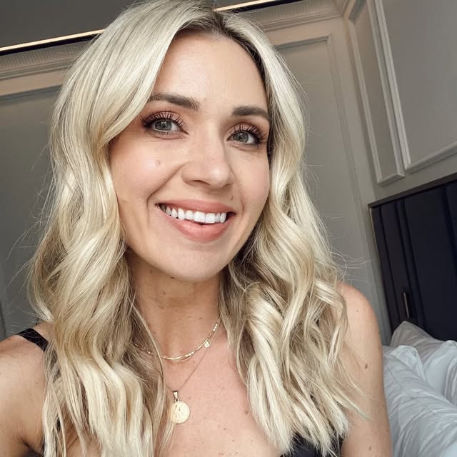 Woman with blonde wavy hair and gold necklace.