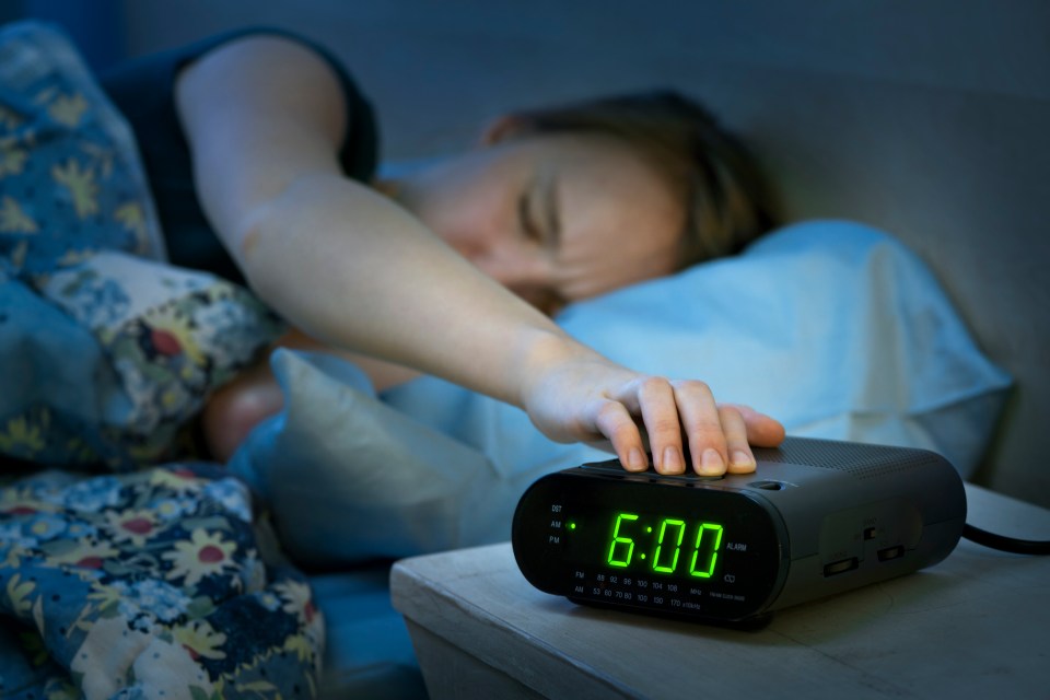 Woman's hand hitting snooze button on alarm clock.