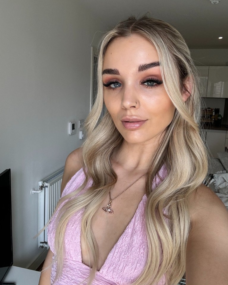 Woman with blonde hair wearing a pink top and necklace.
