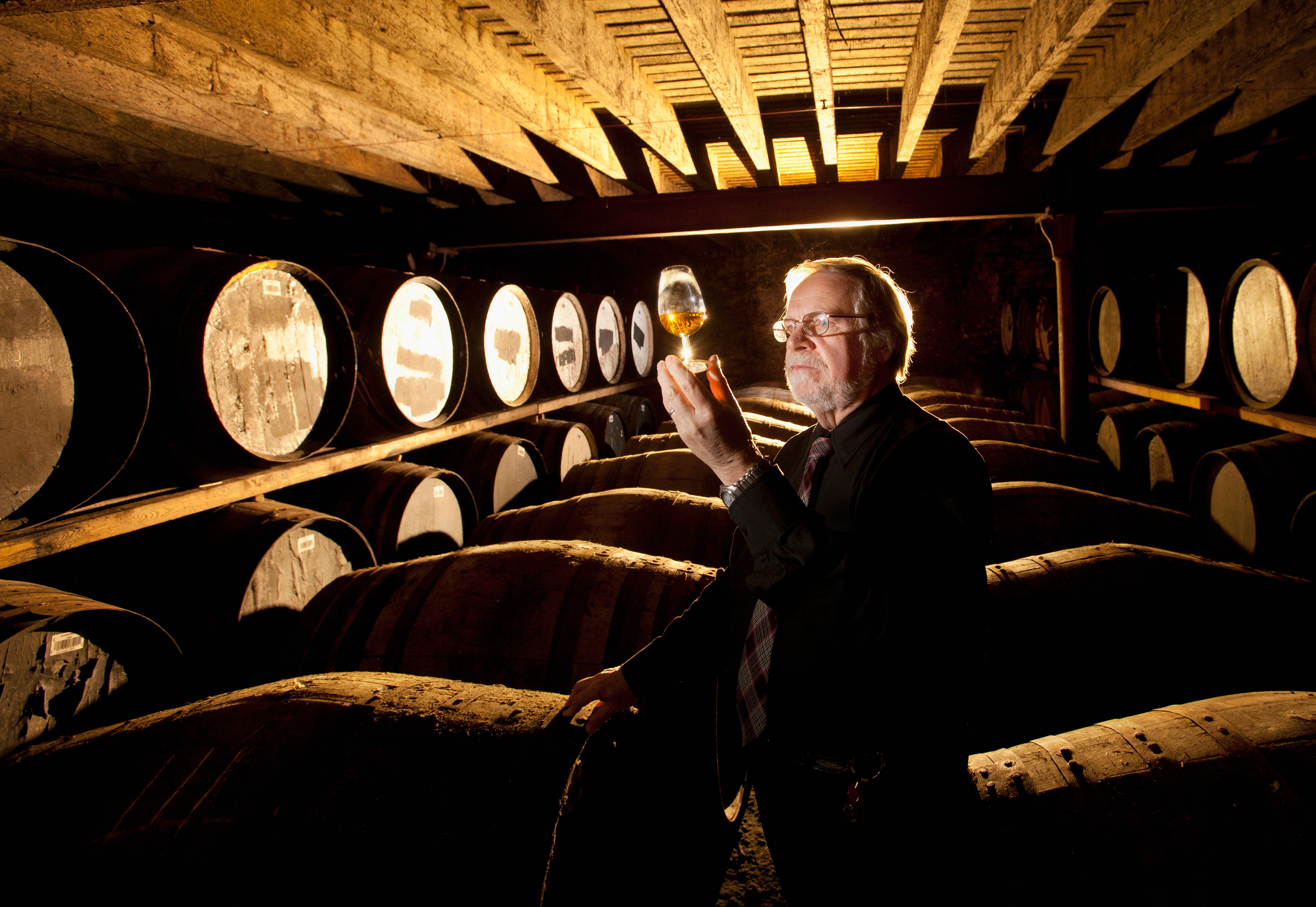 A man inspecting a glass of Scotch whisky in a distillery.