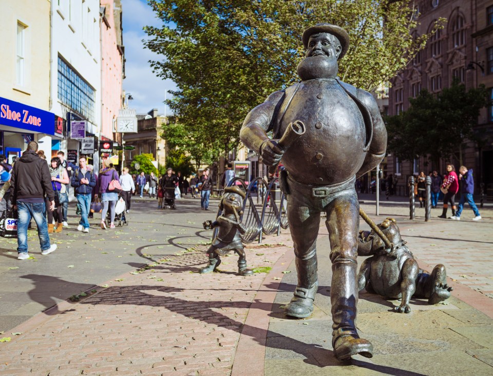 Dundee, Scotland, UK - October 10, 2013: People on Dundee's High Street, passing bronze statues of comic characters Desperate Dan, Dawg, and Minnie the Minx. The characters featured in The Beano and The Dandy, published in Dundee by DC Thomson. Unveiled by schoolchildren in 2001, the statues were created by artists Tony and Susie Morrow.