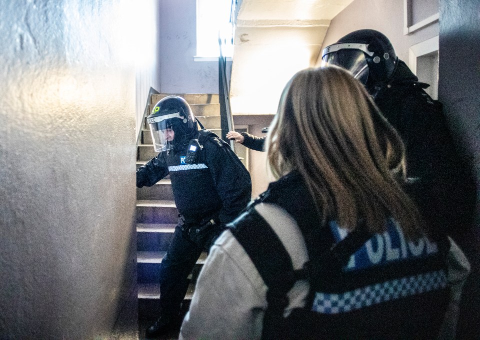 Police officers in riot gear ascending a stairwell during a raid.