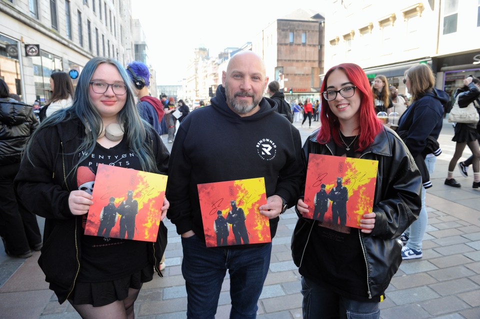 Three people holding autographed Twenty One Pilots albums.