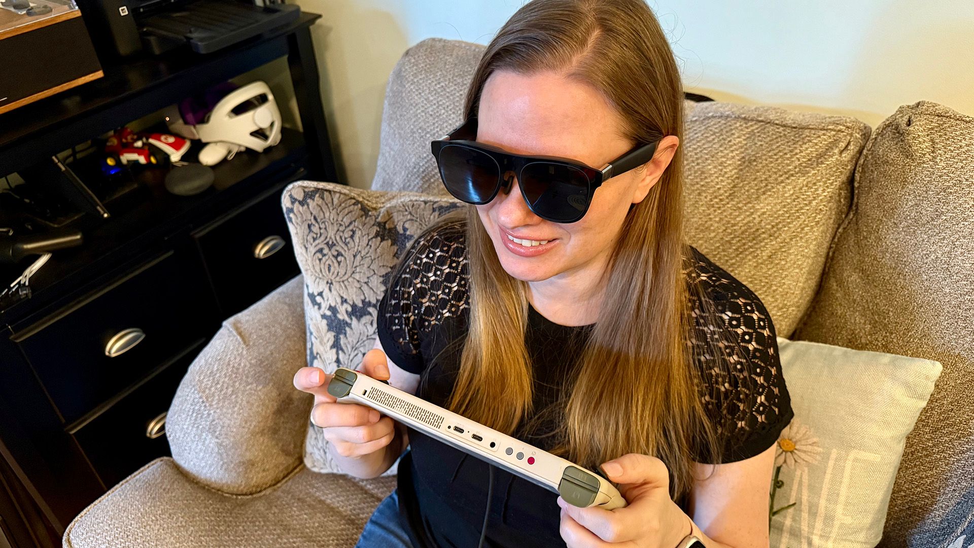 A woman playing on a handheld gaming PC while wearing the XREAL One AR Glasses.