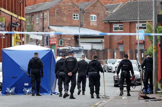 GMP officers at the scene of a double stabbing in Salford which has left one man fighting for his life. 