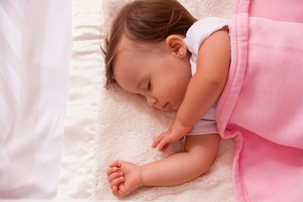 Baby girl sleeping on her side with a pink blanket over her