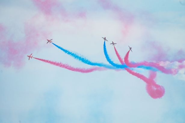 Five small planes in the sky leaving trails of red and blue smoke