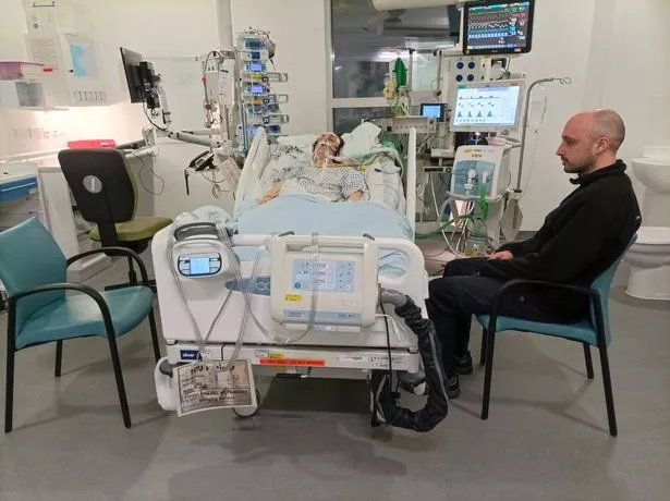 Anna lying in a hospital bed in the ICU while her brother sits beside in a chair