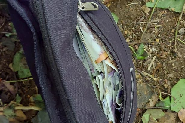 A black fabric bag stuffed with lots of £10 and £20 notes