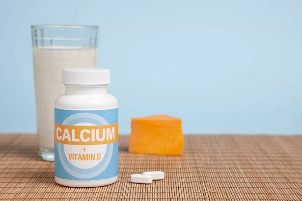 Calcium bottle and generic label on a table. Other sources of calcium, milk and cheese, are in the background along with copy space.