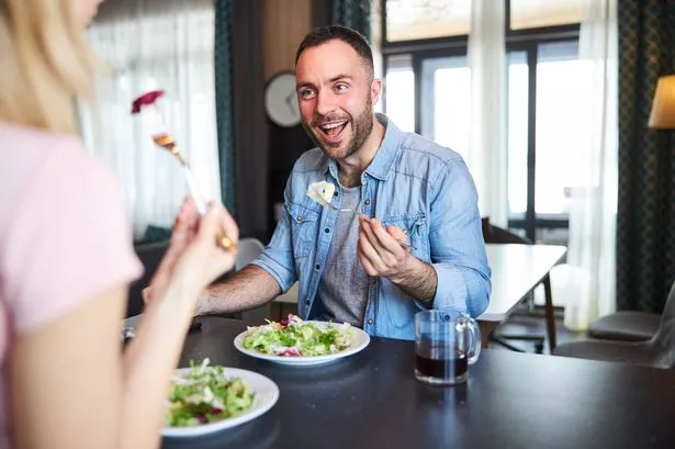 Handsome gentleman eating salad and laughing while sitting at the table and talking with lady