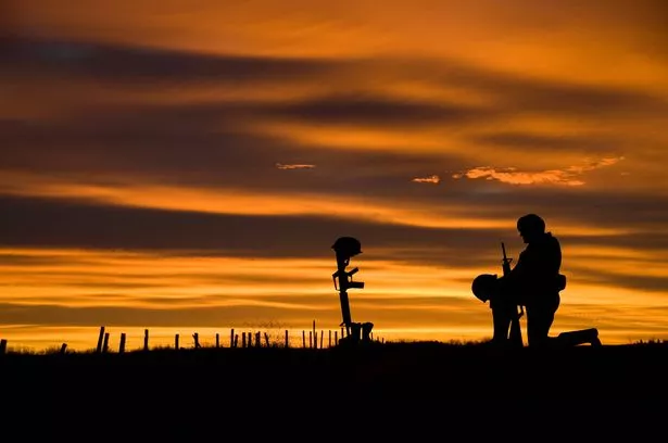 The battlefield grave of a fallen soldier with another soldier kneeling before it. Copy space
