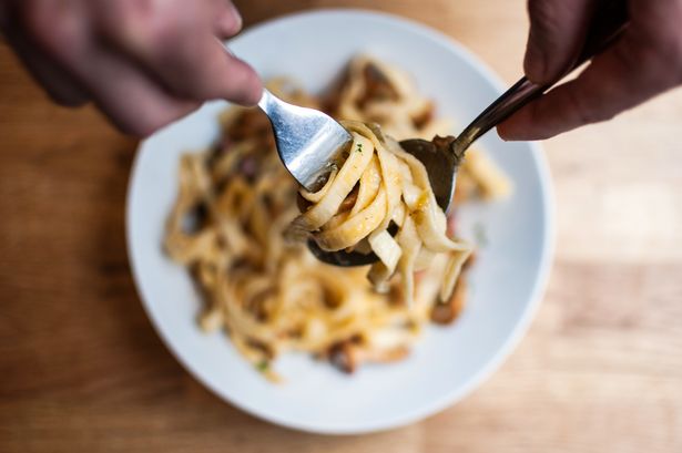A high angle closeup shot of a person reeling up the pasta with a spoon and a fork