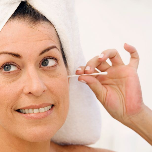 Woman in towel uses cotton bud to clean ear