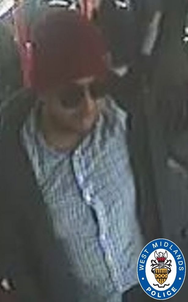 CCTV image of a white man who is wearing a red beanie hat and large sunglasses and a white and blue checked shirt and a dark jacket