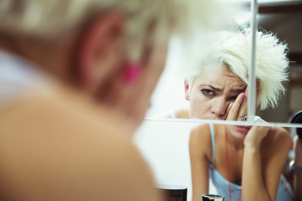 Woman examining her complexion in the mirror. Hang over. Generic Image