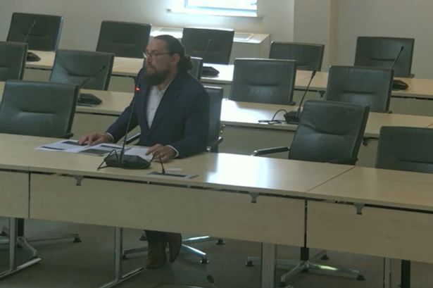 Man with beard and glasses sat at desk at council meeting