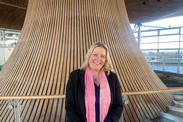 A woman in a pink scarf in front of a wooden structure