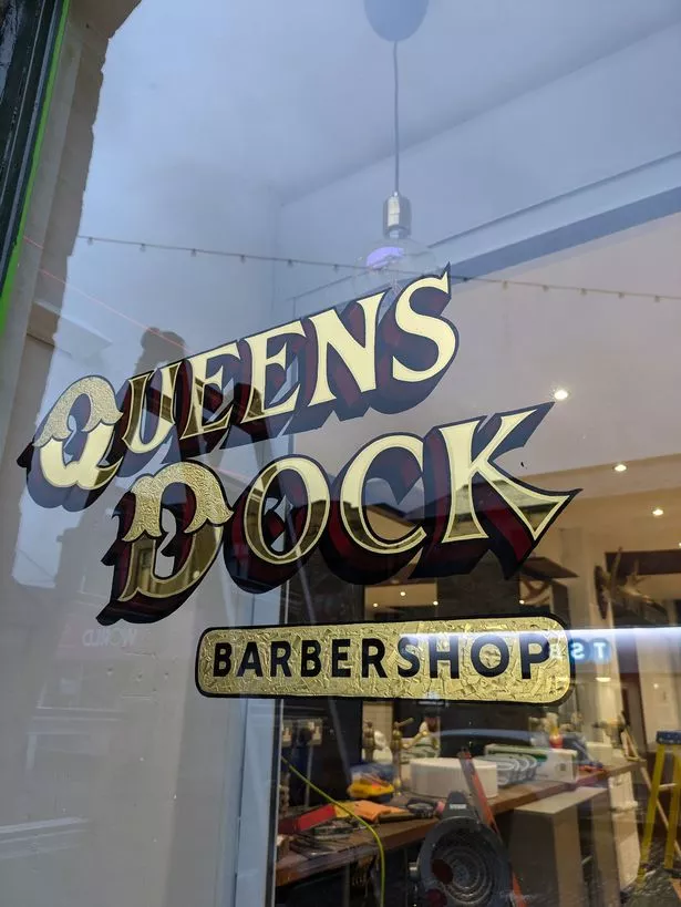  A gold sign reading 'Queens Dock Barbershop'.