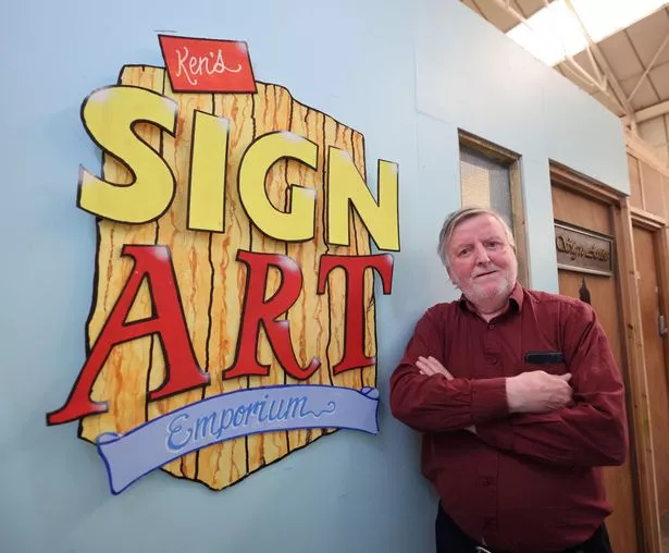 This photo shows Ken Bullock standing in front of a sign reading 'Sign Art Emporium'