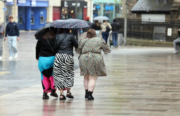 Three people walking through the rain in Cardiff city centre with umbrellas