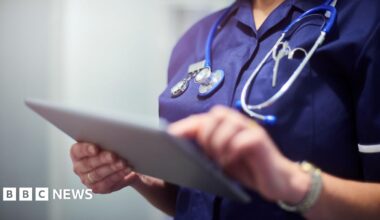 A close up image of a medical professional typing on a tablet with a stethoscope around her neck. You cannot see her face.