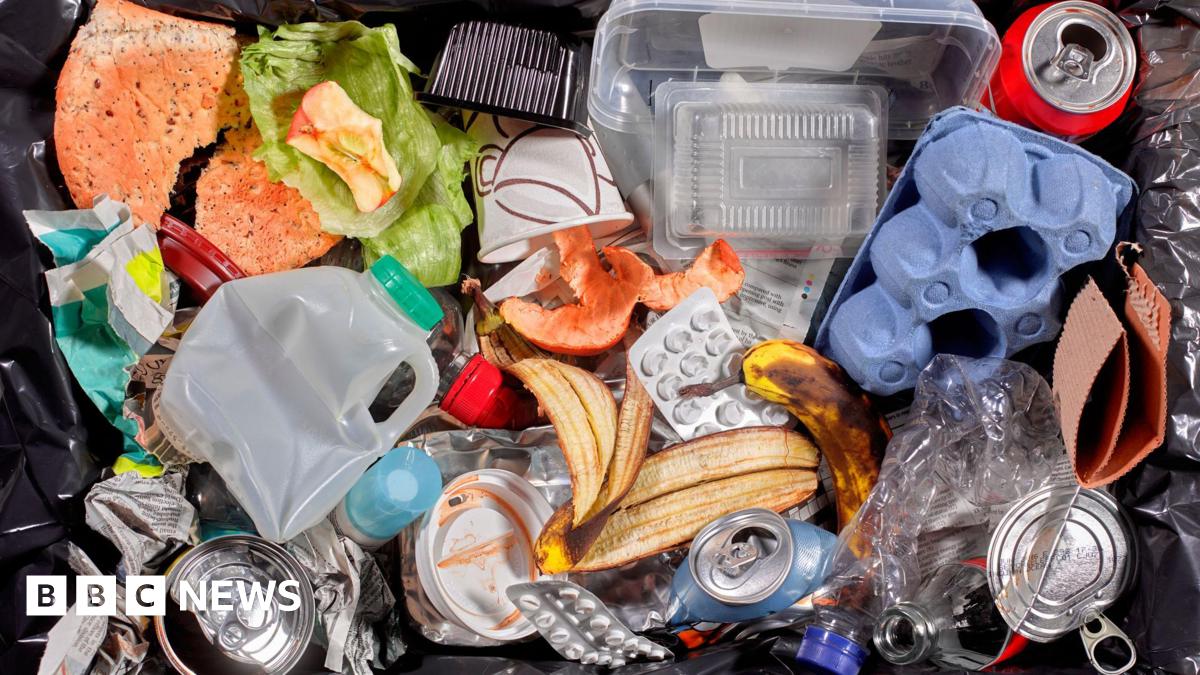 A bin filed with household waste, such as empty milk bottles and banana skins
