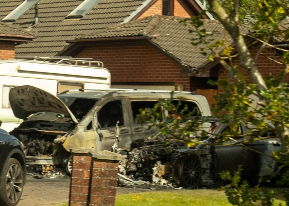 Two burnt-out cars in front of a house.