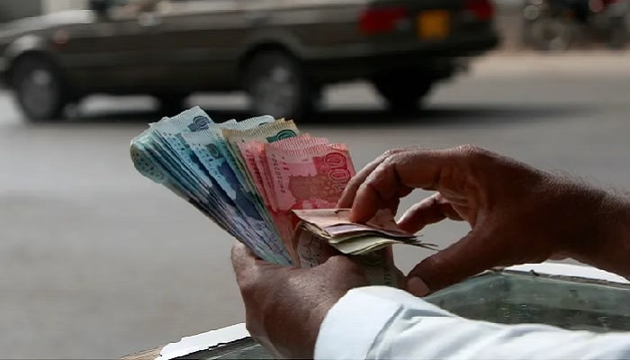 A roadside vendor counts rupee notes in Karachi. — Reuters/File