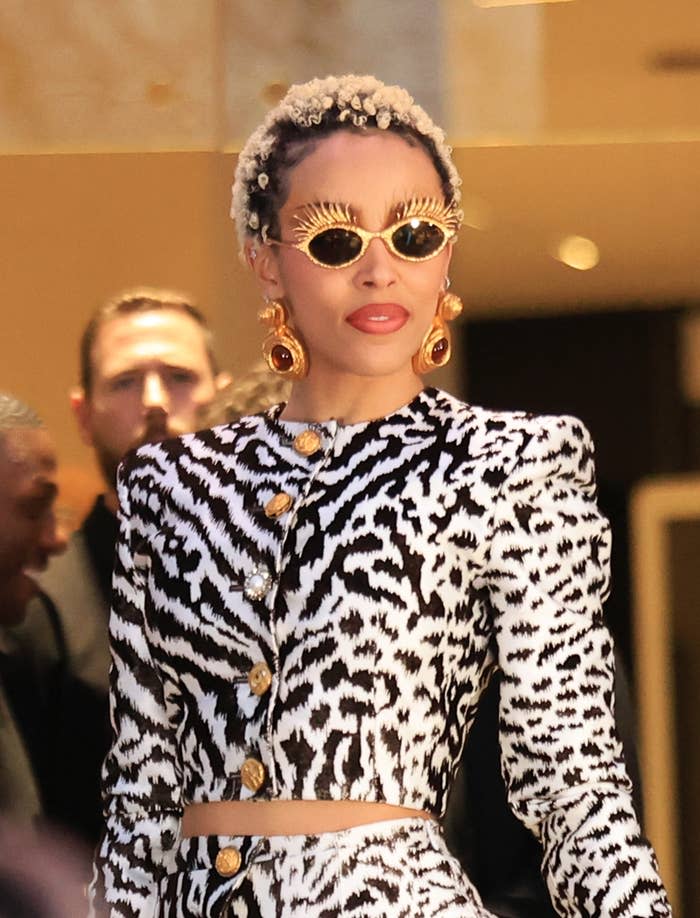 Person in a bold-patterned outfit with striking sunglasses and large earrings, attending an event
