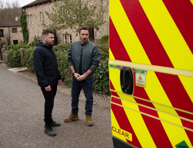 Aaron Dingle and John Sugden standing outside an ambulance in Emmerdale.