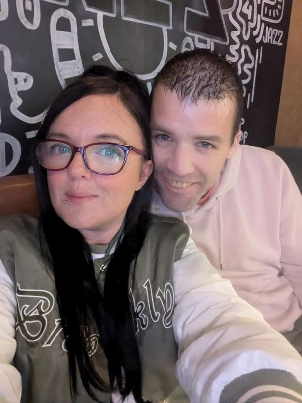 An image of a dark-haired woman with glasses and a green top sitting next to a dark-haired man wearing a pink shirt.