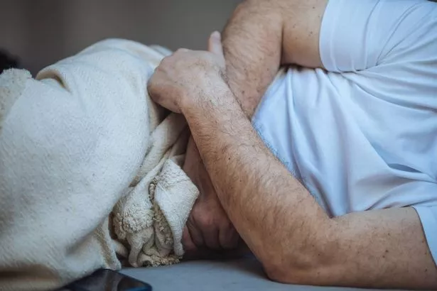 An unrecognizable man is suffering from abdominal pain lying on the bed crossed his arms in the stomach