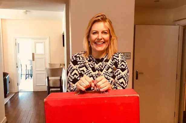 A woman in a black and white top holding a red box as used by government ministers