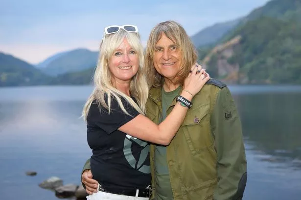 Couple in their 50s/60s. A woman with blonde hair has her arms around a man with blonde hair 